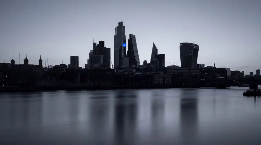 The City of London skyline at blue hour from across the Thames, one window lit blue.