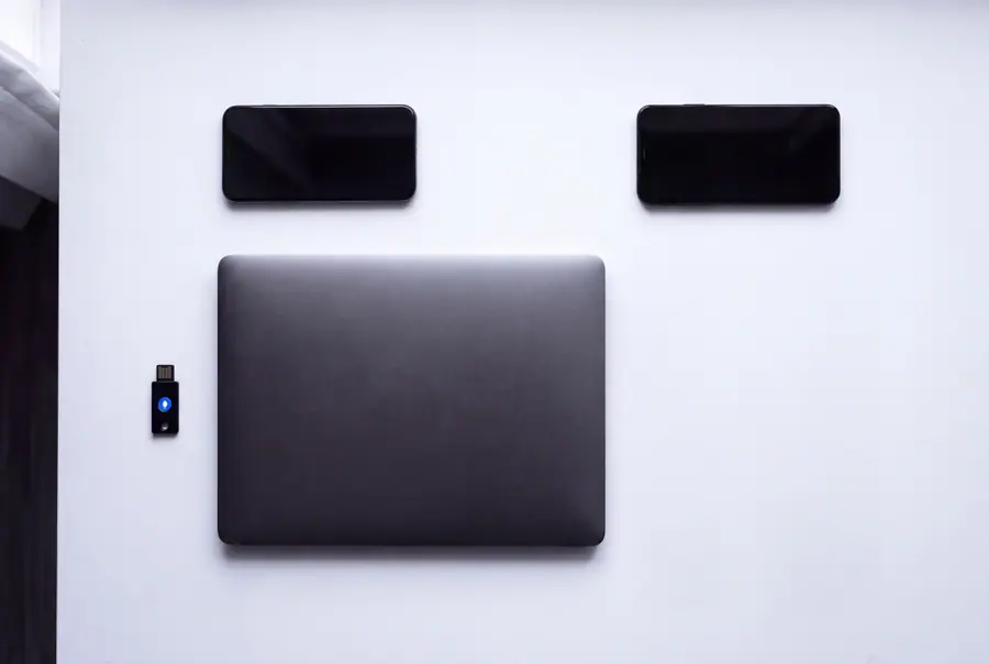 Phones, a laptop and a hardware security key laid out in a grid on a white desk for device enrolment.